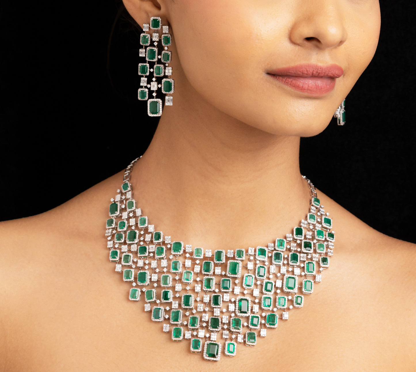 Woman wearing a green emerald necklace and earrings on a black background